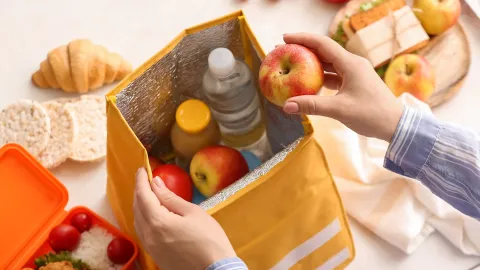 Bag being loaded with apples and bottled drinks, other food visible in background