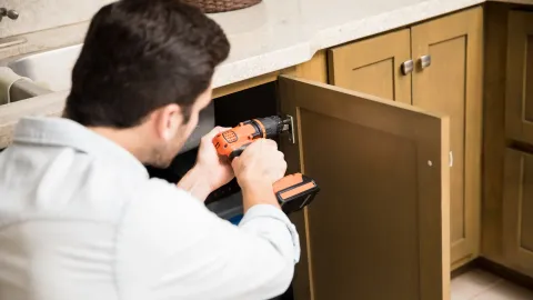 Man fixes under counter cabinet with drill
